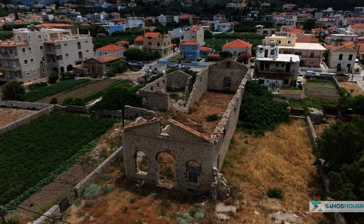 Aerial view of the SH589 plot's ruined stone building among the houses of Karlovasi, Samos