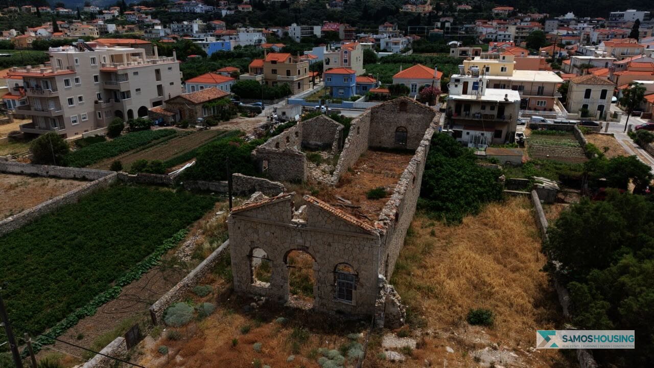 Aerial view of the SH589 plot's ruined stone building among the houses of Karlovasi, Samos